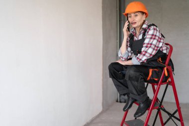 Kadın inşaat işçisi ya da inşaatçı merdivende otururken akıllı telefondan arıyor. meslek, inşaat ve inşaat kavramı.