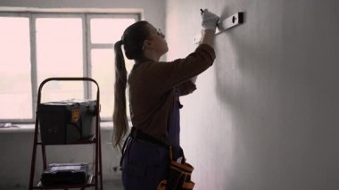 Ev yenileme ve yenileme konsepti. Duvarı ruh seviyesiyle ölçen kadın tamirci oturma odasında tadilat yapıyor. Boşluğu kopyala