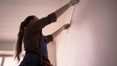 Genç bir kadın ev onarımı yapıyor, duvarları bant cetveliyle ölçüyor. Onarım, inşaat ve ev yenileme konsepti