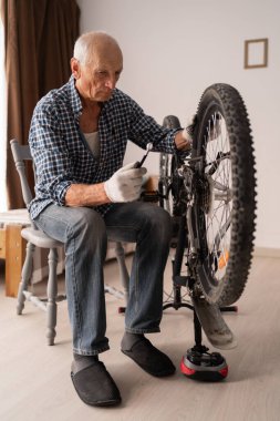 Aktif kıdemli adam evde bisiklet tamir ediyor. Boş vakitlerde bisiklet sürmek. Bisiklet bakımı için ekipmanı olan emekli erkek tamirci. Boşluğu kopyala