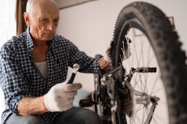Aktif kıdemli adam evde bisiklet tamir ediyor. Boş vakitlerde bisiklet sürmek. Emekli erkek tamirci. Bisiklet tamircisi. İngiliz anahtarıyla tamir tekerleği.