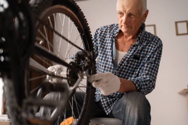 Aktif kıdemli adam evde bisiklet tamir ediyor. Boş vakitlerde bisiklet sürmek. Bisiklet bakım tekerlerini tamir etmek için ingiliz anahtarıyla çalışan emekli bir tamirci. Yakın plan.