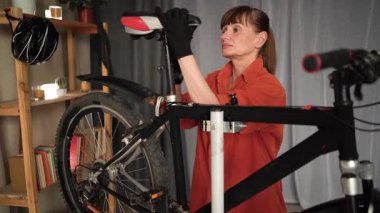 Orta yaşlı bir kadın ev onarımı sırasında bisiklet koltuğu takıyor ve çerçevesini sağlamlaştırıyor. Oturma düzeni, bisiklet restorasyonu ve DIY ev bakımı kavramı.