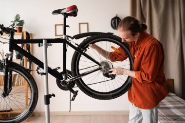 Focused long haired man fixing bicycle at home, using a spanner wrench for checking wheels. bike maintenance.
