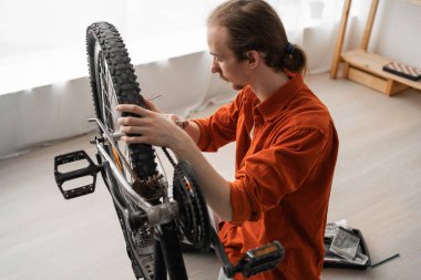 Young man repairing bicycle fixing wheels with wrench at home. high angle