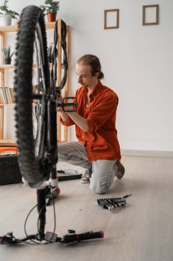 young hipster repairing bicycle at home preparing his bike for summer season. apartment interior with repairman