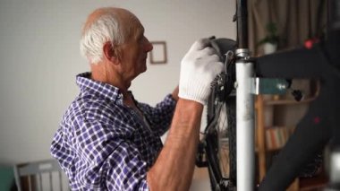Elderly man fixing bicycle at home, tightening fender on wheel using wrench. Concept of maintenance, fixing, repair and preparing bicycle for new season. Copy space