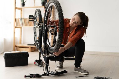 Caucasian girl examines the front wheel of her bicycle at home. Troubleshooting, maintenance, hobby, women's leisure. bicycle repair at home, banner, copy space.