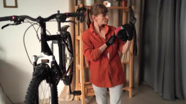 Orta yaşlı bir kadın tamirden önce evde bisiklet koltuğunu kontrol ediyor. Hasar teftişi, kapalı alanda değerlendirme ve bisiklet ekipmanları bakımı kavramı.