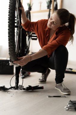 Young lady repairing a bicycle: carefully examining the wheel. Home workshop, passion for sports, active lifestyle.
