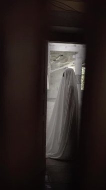 Beyaz çarşaflı cadılar bayramı hayaleti, terk edilmiş bir binada örümcek ağlarıyla dikiliyor. Korku konsepti. Dikey görünüm