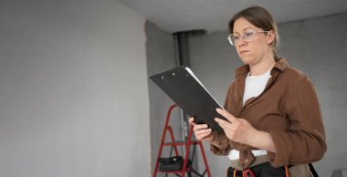 repairwoman doing home repairs DIY stands in the room holding a clipboard. Banner. Copy space