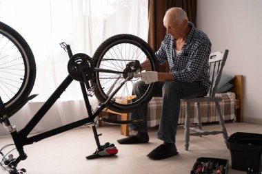 Yaşlı bisikletçi evde bisikletini tamir ediyor. Diy konsepti. Motor bakımı