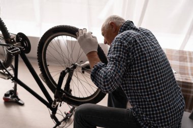 Emekli aktif adam evde bisiklet tamir ediyor. İngiliz anahtarlı bisiklet bakımı. Boşluğu kopyala