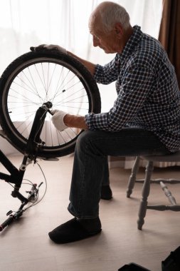 Aktif son sınıf erkek bisikletçi ingiliz anahtarıyla bisiklet tekerleğini kontrol ediyor. Evde hasarlı bisiklet tekerleği var. Boşluğu kopyala