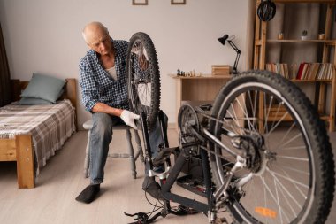 Aktif kıdemli adam evde bisiklet tekerleği ve zinciri ayarlıyor. Bisiklet tamiri, bakım onarımı. Bisiklet hobisi. Boşluğu kopyala