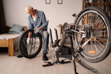 Evde bisikleti tamir eden yaşlı bir adam sandalyede otururken bisiklet direksiyonu tutuyor. Bisiklet ve DIY onarım kavramı