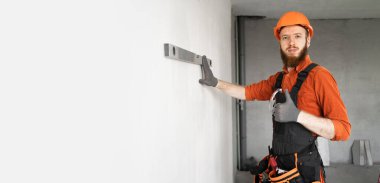 Tamir ve inşaat konsepti. Erkek müteahhit ya da koruyucu miğferdeki inşaat mühendisi duvarı düzgünce ölçer. İnşaat işçisi duvarı kontrol ediyor. Pankart. Boşluğu kopyala