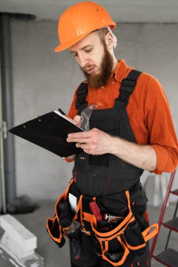 İnşaatçı inşaat işçisi. Alet kemeri ve kaskında inşaat alanında ya da yeni bir evde pano var. Yakın plan.