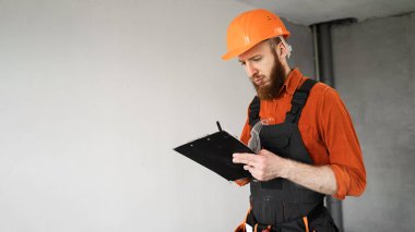 Tamir, inşaat ve inşaat kavramı. Yeni evin içinde gri duvarın yanında kask takan bir inşaat işçisi. Pankart. Boşluğu kopyala