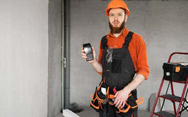 Maaş konsepti. Banka ödeme terminalini tutan mavi tulumlu inşaatçı ya da tamirci. Boşluğu kopyala