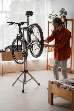 Bisikletini tamir eden ve tamir eden genç adam yaz bisiklet sezonu için aracı hazırlıyor. Boşluğu kopyala