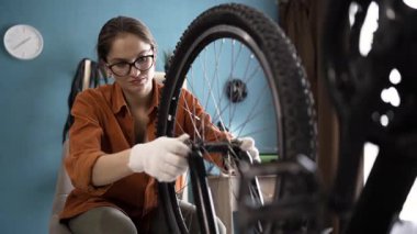 Evde bisiklet tamiri sırasında vidaları sökmeye hazırlanan gözlüklü genç bir kadın. Boşluğu kopyala