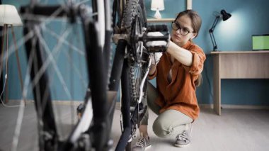 Evde bisiklet tamir ederken direksiyonu kontrol eden genç bir kadın. Boşluğu kopyala