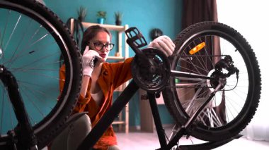 Evde bisikletini tamir eden bir kadın tamirciyi arayıp bisikletini tamir etmek için yardım istiyor. Boşluğu kopyala