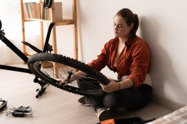 Evde yerde otururken bisiklet tamir ve onarım işleri yapan genç bir kız öğrenci. Boşluğu kopyala