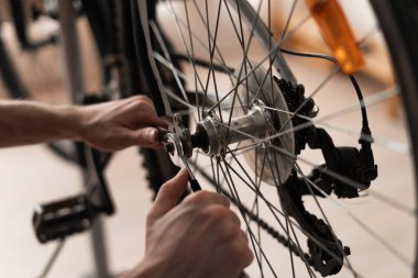 Arka tekerlek dingilini ve merkezini sıkılaştırmak için iki anahtar kullanarak evde bisiklet tamir eden ellerin yakın çekimi. Ev bakımı, teknik ayar ve DIY motor servisi kavramı.