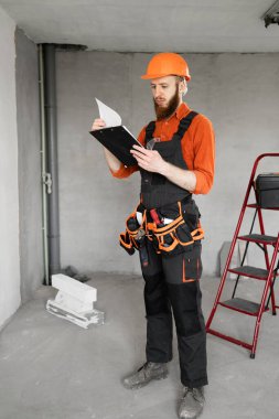 İnşaatçı inşaat işçisi. Alet kemeri ve kaskında inşaat alanında ya da yeni bir evde pano var. Boşluğu kopyala.