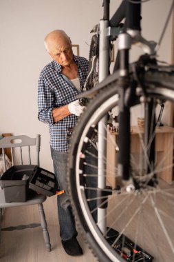 Oturma odasında bisikleti tamir eden kıdemli adam yaz için hazırlanıyor. Kapalı yer taşıma, mevsimsel onarım ve olgun ev tamircisi kavramı. Kopyalama alanı olan pankart