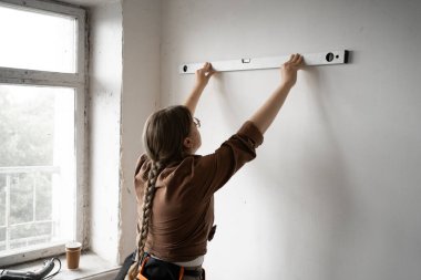 Yakın plan kadın tamirci ev onarımı sırasında ruh seviyesini kullanarak duvarı ölçüyor. İşçiliği, hassasiyeti, ev gelişimini ön plana çıkarıyor. Boşluğu kopyala