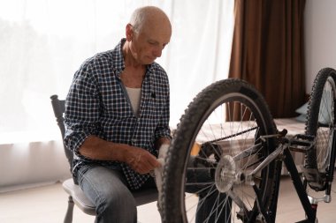 Evde bisiklet tamir eden gömlekli yaşlı bir adam. Kendin yap bisiklet tamiri ve bakım konsepti