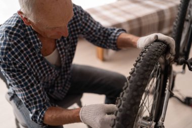 Yaşlı adamın evde günlük kıyafetlerle bisiklet tamir edişinin en üst görüntüsü. Motosiklet bakım ve onarım konsepti