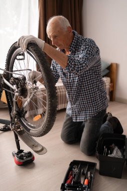 Yaşlı adam bisiklet anahtarıyla ev atölyesinde bisikleti kontrol ediyor. Bisiklet servisi ve tamir konsepti
