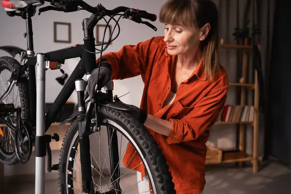 Turuncu gömlek giyen orta yaşlı bir kadın evde bisiklet frenlerini tamir ediyor. Boşluğu kopyala