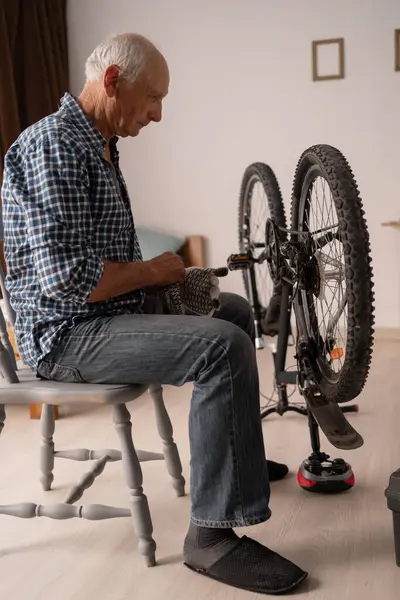 Emekli adam evde bisiklet tamir ediyor oturma odasında sandalyede oturuyor, DIY ve hobiler konsepti