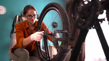 Gözlüklü bir kadın bisiklet tekerleği monte ediyor, evde bisiklet bakım servisi yapmak için onu söküyor. Boşluğu kopyala