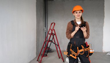 Miğferli genç İspanyol kadın işçinin portresi inşaat aşamasındayken işe ara verirken akıllı telefon kullanıyor. Boşluğu kopyala