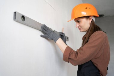 Ciddi kadın müteahhit duvarında ruh seviyesiyle ölçüm yapıyor. Boşluğu kopyala