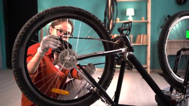 Bisikleti tamir eden genç bir kadın bisiklet tekerleğindeki zinciri kontrol ediyor. Boşluğu kopyala