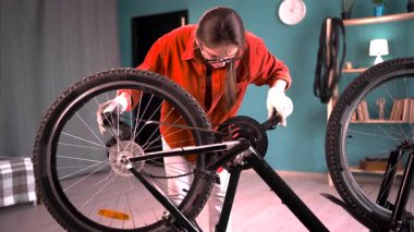 Gözlüklü genç bir kadın bisiklet tamir ediyor. Bisiklet sürerken zincir kontrolü yapıyor. Boşluğu kopyala