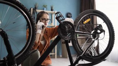 Gözlüklü, bisikleti tamir eden genç bir kadın akıllı telefon kullanarak danışmanlık için tamirciyi arıyor. Boşluğu kopyala