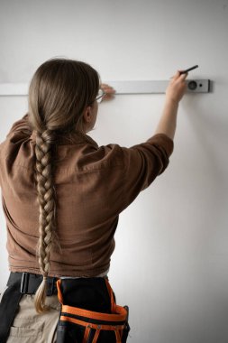 Yakın plan kadın tamirci ev onarımı sırasında ruh seviyesini kullanarak duvarı ölçüyor. İşçiliği, hassasiyeti, ev gelişimini ön plana çıkarıyor. Boşluğu kopyala
