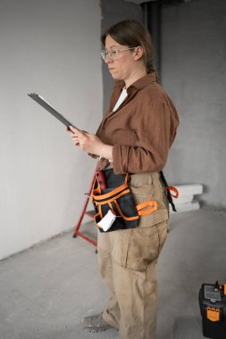 Ev ya da apartman yenileme sırasında tamamlanmamış odada çalışan kadın inşaat işçisi panosu. Boşluğu kopyala