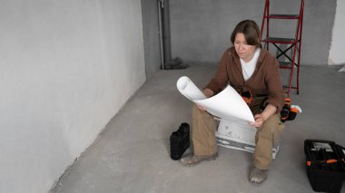 Tamirci kadın, tadilattan önce Bitmemiş Oda 'da oturuyor. Yüksek açı. DIY ev bakımı kavramı