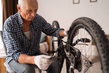 Aktif kıdemli adam evde bisiklet tamir ediyor. Boş vakitlerde bisiklet sürmek. Bisiklet bakım tekerlerini tamir etmek için ingiliz anahtarıyla çalışan emekli bir tamirci. Boşluğu kopyala