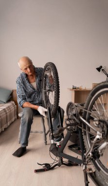 Aktif kıdemli adam evde bisiklet tekerleği ve zinciri ayarlıyor. Bisiklet tamiri, bakım onarımı. Bisiklet hobisi. Boşluğu kopyala